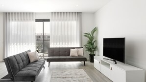A modern living room with a grey sofa, a matching ottoman, a large flat-screen TV, and a potted plant.