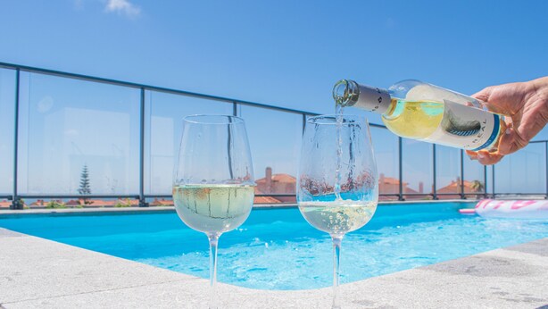 Two glasses of white wine on a poolside table with a clear blue sky in the background.