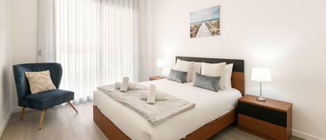 A modern bedroom with a large bed, a chair, a nightstand, and a painting on the wall.