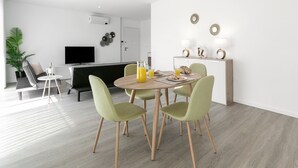 A modern living room with a dining area, a flat-screen TV, and a coffee table with drinks.