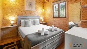 Ein gemütliches Schlafzimmer in einer Holzhütte mit Bett, Nachttischlampen, einem Fenster und einem Kopfteil.