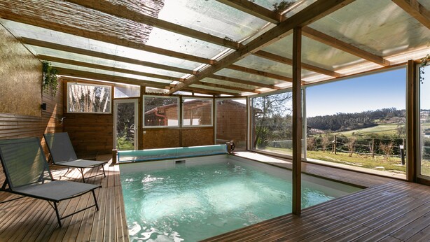 Eine Holzterrasse mit Pool, Liegestühlen und großen Fenstern mit Blick auf die Landschaft.