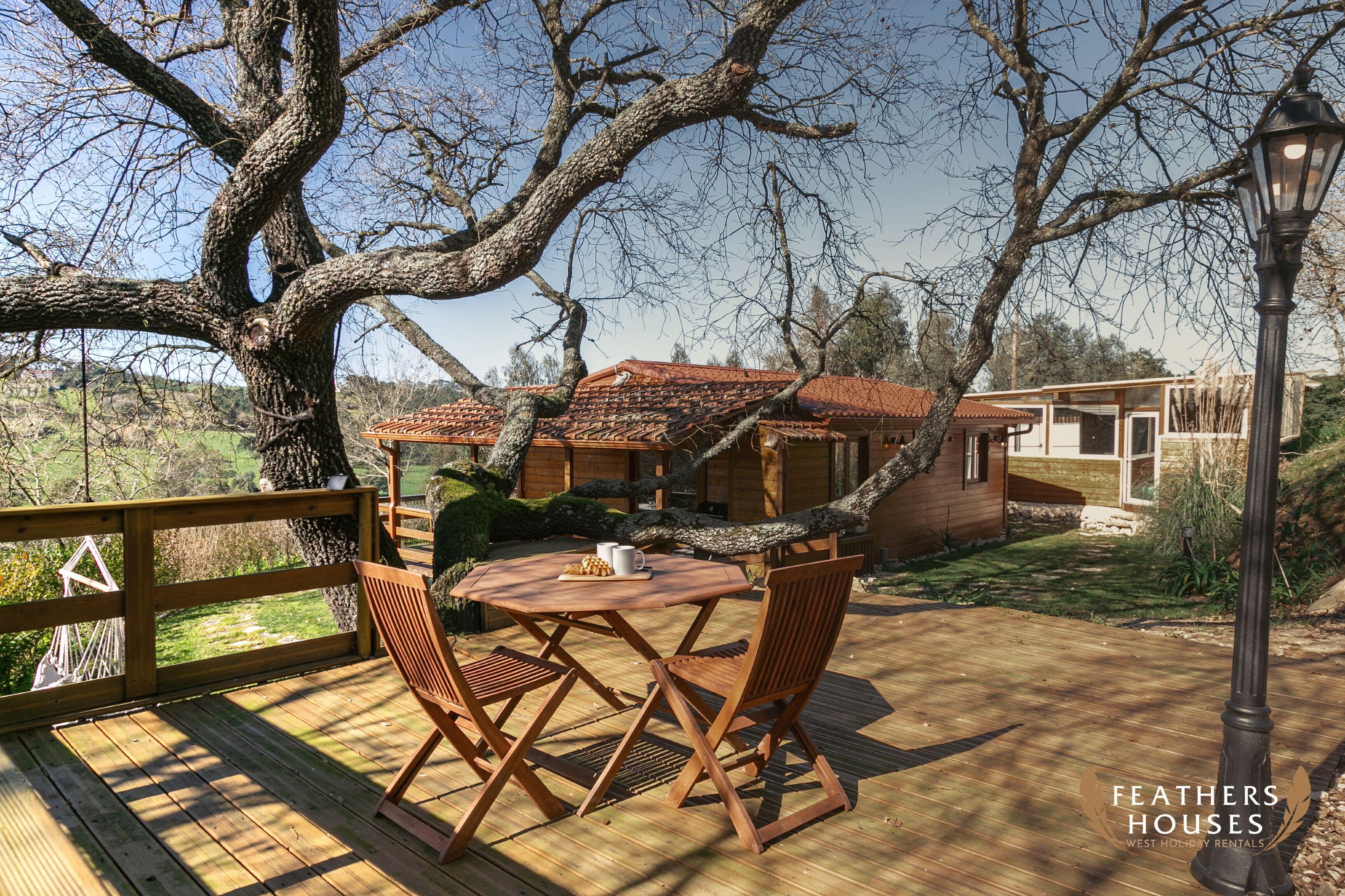 A wooden deck with a round table and chairs, overlooking a house with a red roof.