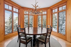 Una habitación con paneles de madera, una mesa redonda y sillas, ventanas amplias y un candelabro.
