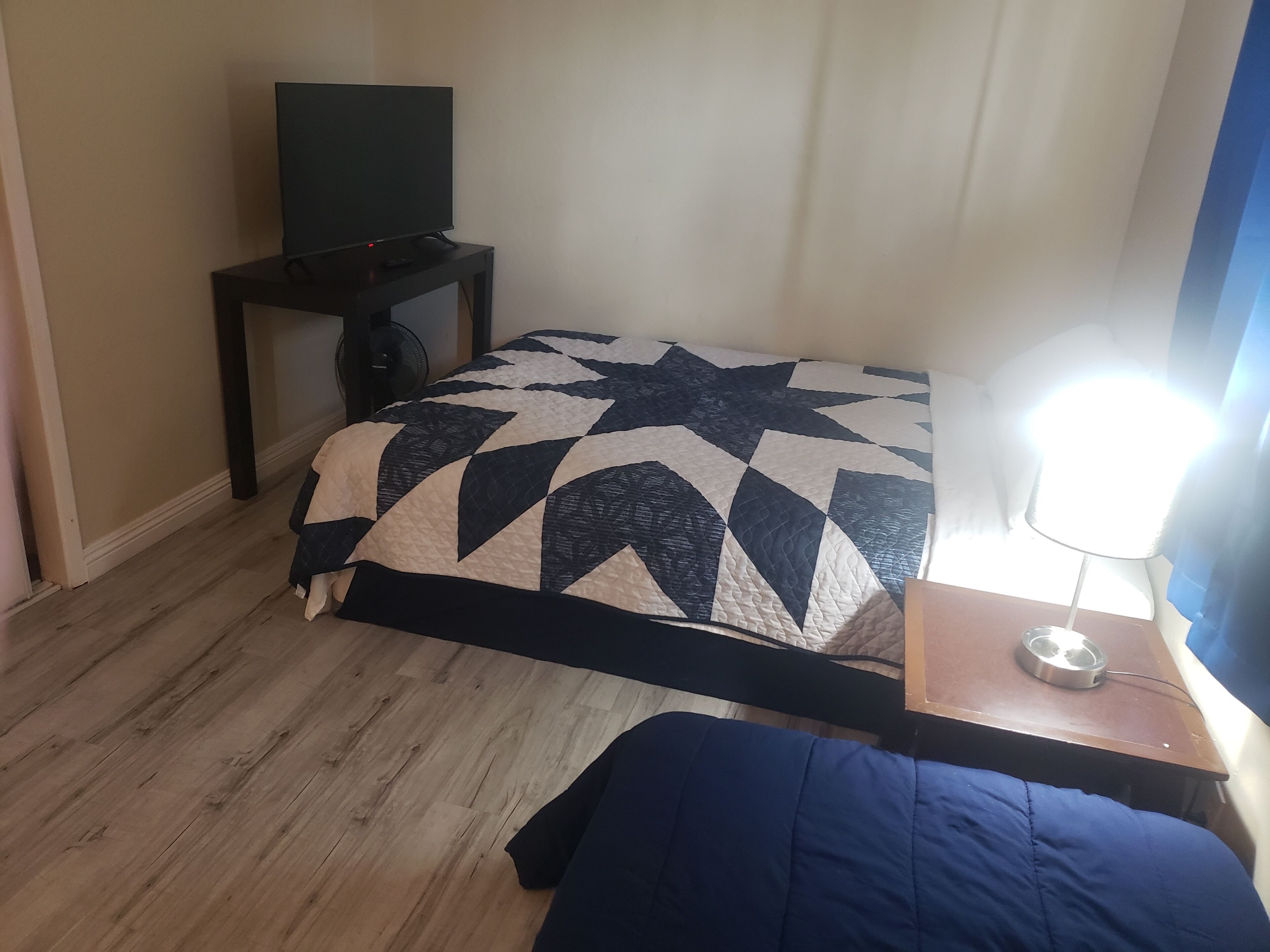Een hotelkamer met een bed, een televisie op een standaard, een nachtkastje met een lamp en een houten vloer.