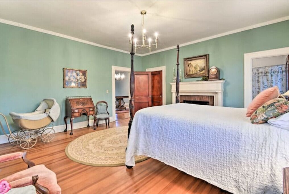Une chambre à coucher avec un grand lit, un lustre, une cheminée et un vieux carrosse.