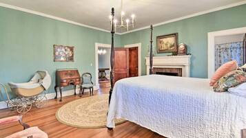 Une chambre à coucher avec un grand lit, un lustre, une cheminée et un vieux carrosse.