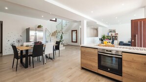 A modern kitchen with a central island, a dining area with a wooden table and chairs, and a staircase leading to an upper level. - Aromas de Alcala Alcalá La Real by Ruralidays (Jaén)