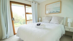 Un lit bien fait, avec une couette blanche et des oreillers, une table de chevet avec une lampe et une fenêtre avec des rideaux.