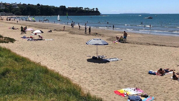 Une plage où l’on voit des gens se prélasser au soleil, des parasols et des bateaux sur l’eau.