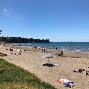 A beach with people sunbathing, umbrellas, and boats in the water.