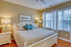 A bedroom with a bed, nightstands, lamps, a ceiling fan, and a window with curtains. - Golf Resort Condo w/ Pool in North Myrtle Beach! (North Myrtle Beach)