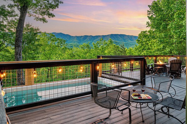 A deck with a pool, chairs, and a table with a fruit platter and wine.