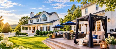 Una casa de dos pisos con terraza, mobiliario exterior y un pérgola.