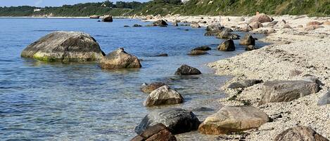 Una playa rocosa con aguas cristalinas y un promontorio boscoso al fondo.