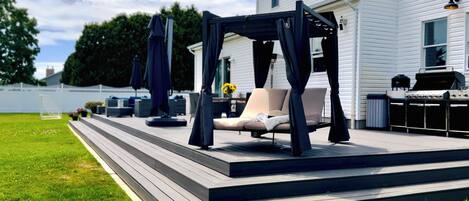 A deck with a canopy, outdoor furniture, and a grill.