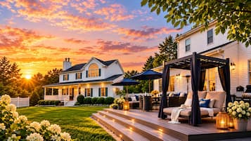 Ein Haus mit überdachter Terrasse, einem gepflegten Rasen und einem Sonnenuntergang im Hintergrund.