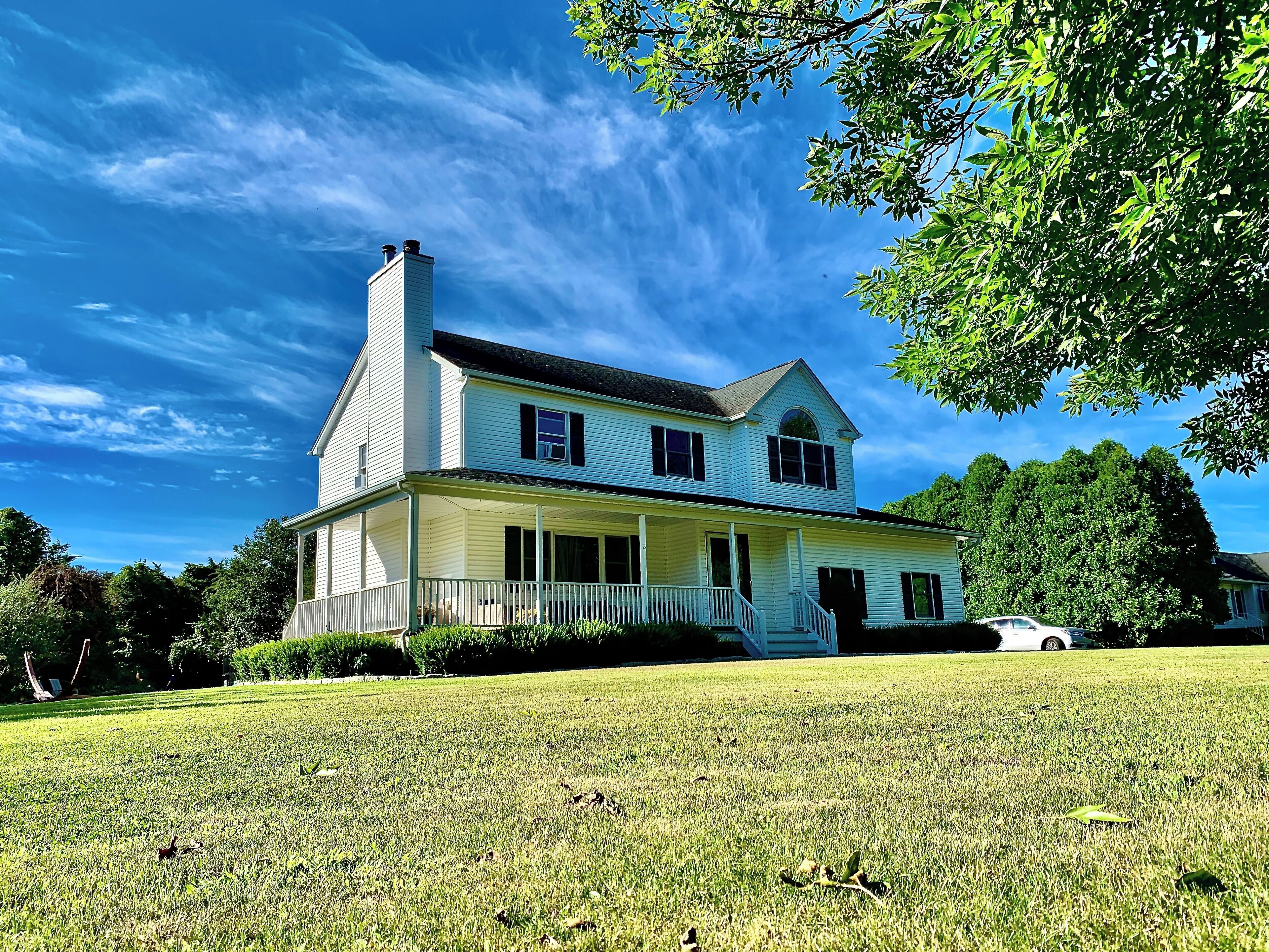 A two-story house with a porch and a chimney, surrounded by a well-maintained lawn and trees.