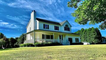 A two-story house with a porch and a chimney, surrounded by a well-maintained lawn and trees.