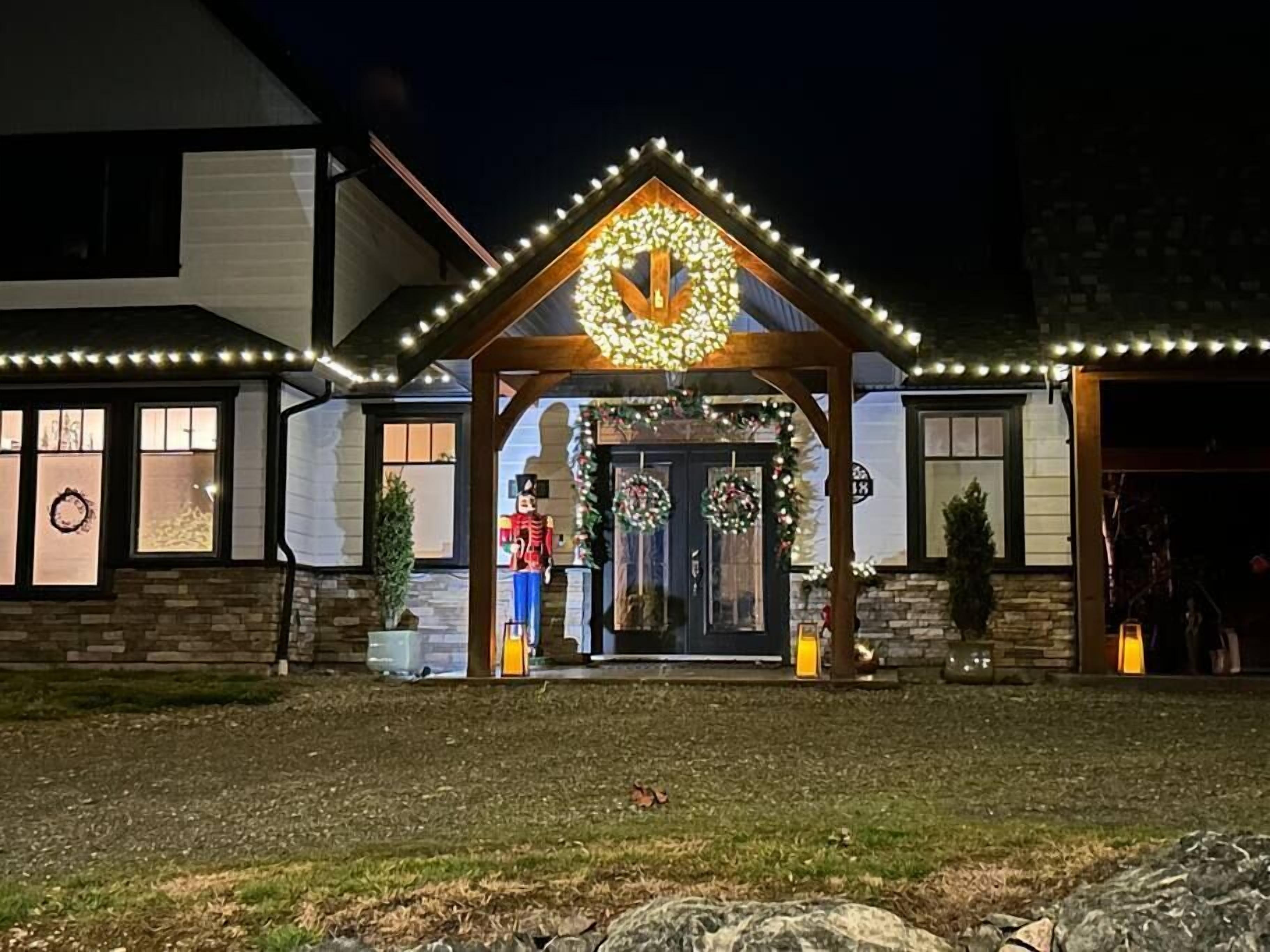 A house with a porch decorated with Christmas lights and wreaths, a nutcracker figure, and a large wreath above the door.