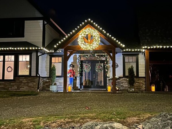 A house with a porch decorated with Christmas lights and wreaths, a nutcracker figure, and a large wreath above the door.
