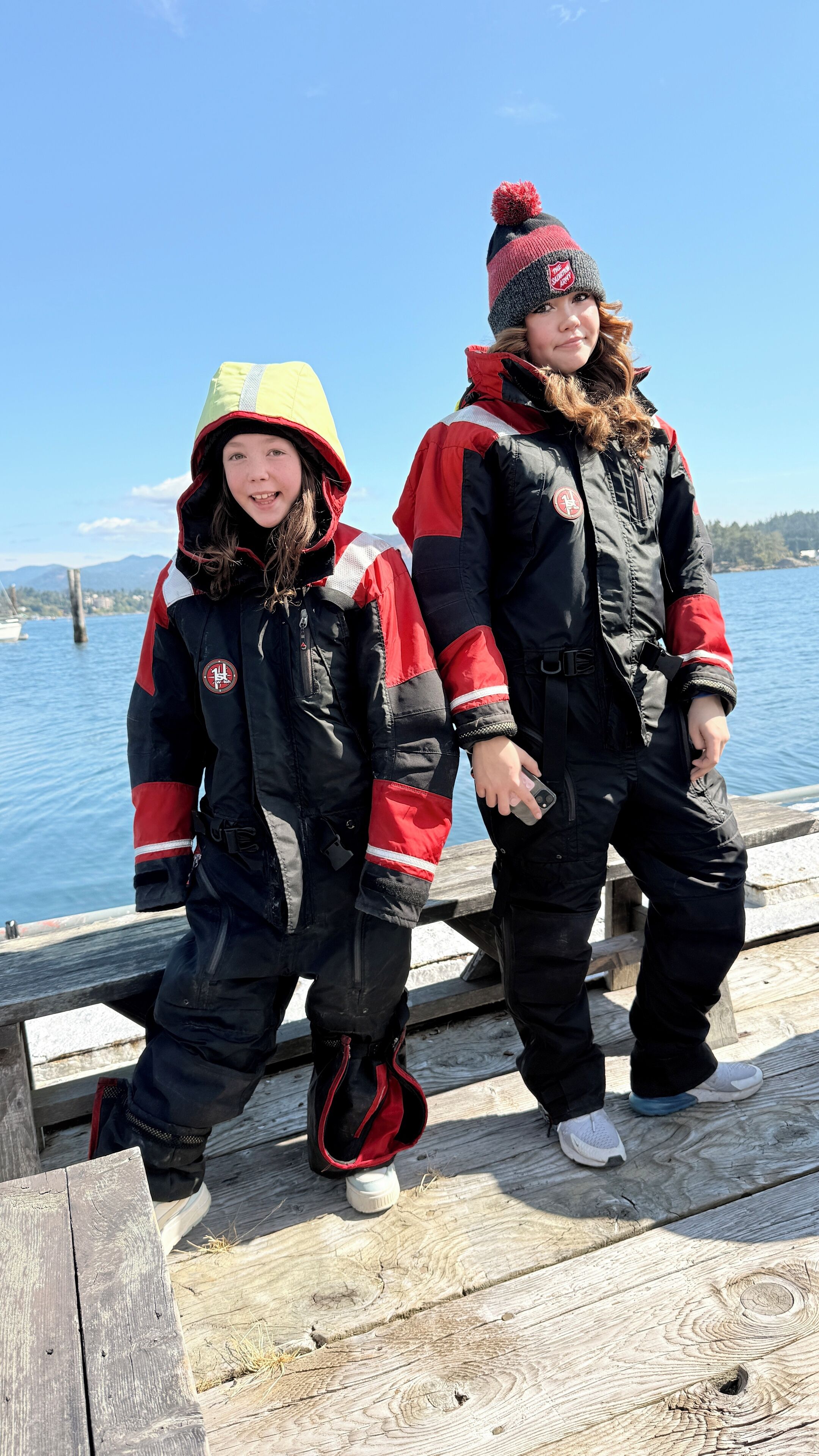 Two individuals in winter clothing standing on a wooden dock by a body of water.