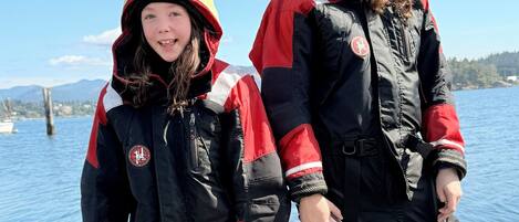Two individuals in winter clothing standing on a wooden dock by a body of water.
