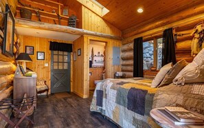 Ein Schlafzimmer in einer Blockhütte mit Bett, Stuhl, Schreibtisch und Fenster.