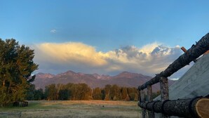 A rustic cabin with a wooden fence and a log in the foreground, set against a backdrop of mountains and a clear sky. - Glamping Tent on the Evans Farm near Joseph, Oregon. (joseph)