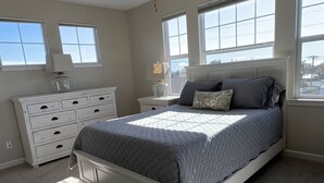 A bedroom with a bed, a dresser, a nightstand, a ceiling fan, and large windows. - Cardiff 5 bedroom home w/pool &  gated driveway near beach (Encinitas)