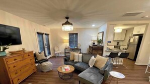 A living room with a sofa, ottoman, coffee table, and a TV. There is a kitchen area with a dining table and chairs. - Blue Bungalow-Downtown Acworth (Acworth)
