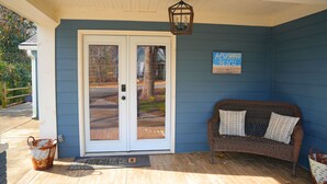 A blue exterior wall with a white door, a wicker sofa with patterned cushions, and a sign reading "ACWORTH BEACH". - Blue Bungalow-Downtown Acworth (Acworth)