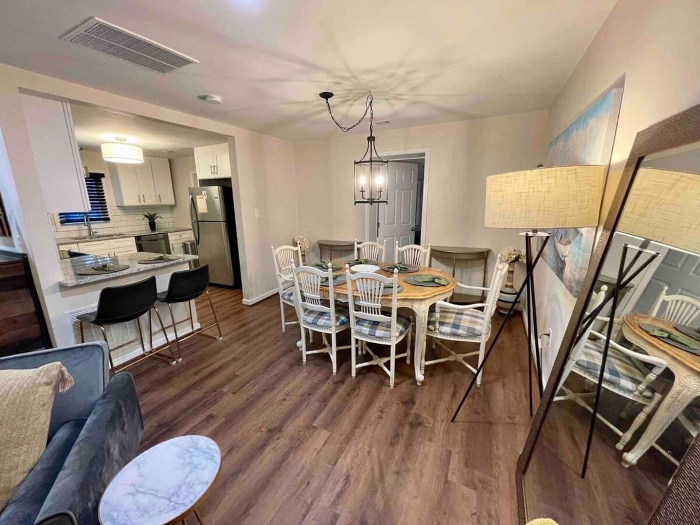 A modern kitchen with white cabinets, a stainless steel refrigerator, and a dining area with a wooden table and white chairs.