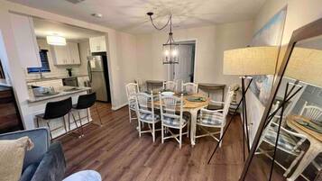 A modern kitchen with white cabinets, a stainless steel refrigerator, and a dining area with a wooden table and white chairs.