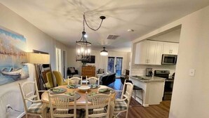 A dining area with a round table, white chairs, and a chandelier. There is a kitchen with white cabinets and a microwave. - Blue Bungalow-Downtown Acworth (Acworth)