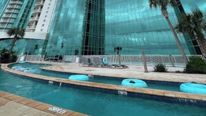 Ett högt hotell med en glänsande glasfasad, en pool med solstolar och palmer.