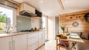 Et moderne køkken med gasblus, indbygget ovn og emhætte. Der er et spiseområde med et bord dækket til to, en sofa og en lille plante i vindueskarmen.