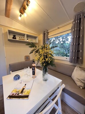 A cozy seating area with a table set for two, a vase with yellow flowers, and a bottle of wine.