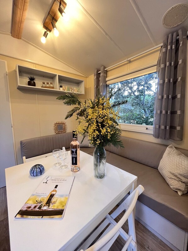 A cozy seating area with a table set for two, a vase with yellow flowers, and a bottle of wine.