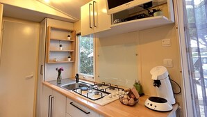 A compact kitchen with white cabinets, a gas stove, a coffee maker, and a flat-screen TV. - The Arbousier, cosy mobile home with sea view (Hyères)