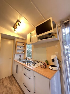 A compact kitchen with white cabinets, a gas stove, a coffee maker, and a flat-screen TV.