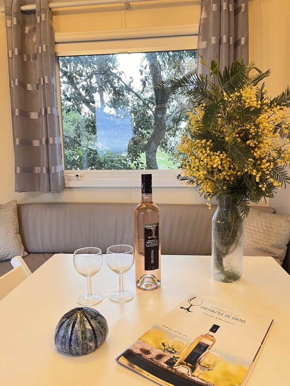 A table with a bottle of Domaine de la Presqu'ile de Giens wine, two wine glasses, a decorative vase with yellow flowers, a small decorative object, and a brochure.