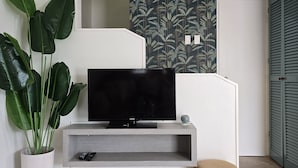 Ein modernes Wohnzimmer mit einem Flachbildfernseher auf einem Holzregal, einer großen Kübelpflanze und einer Wand mit Musterpapier.