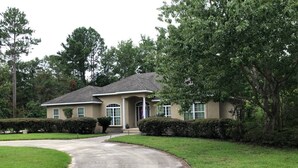 A two-story house with a front driveway, surrounded by well-maintained lawns and mature trees.