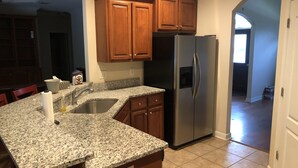 A kitchen with granite countertops, wooden cabinets, a stainless steel refrigerator, and a built-in sink.