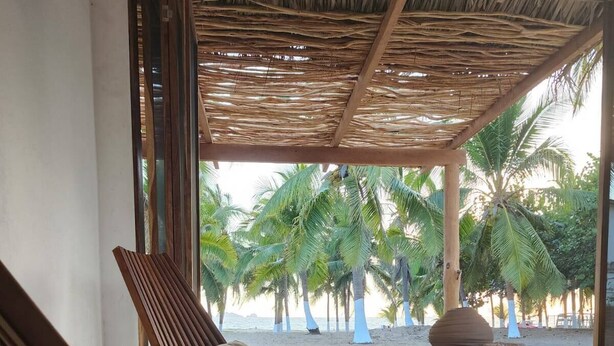 A beachside lounge with wooden lounge chairs and a table, overlooking a palm tree-lined beach.