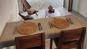 A dining area with a table set for two, a chair, and a view of a sandy beach with palm trees.