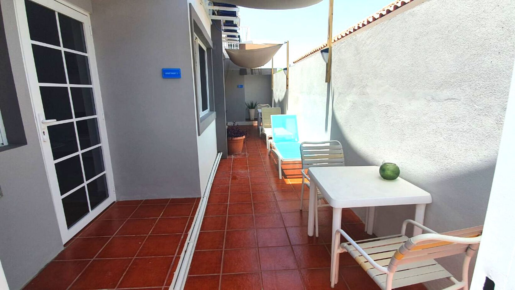A narrow corridor with a white door, a white table with a green object, and a blue chair.