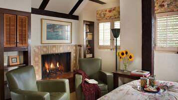 A cozy living room with a fireplace, green leather chairs, a floral bedspread, and a tray with food and drinks.