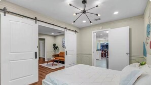 Un dormitorio con cama, puerta corrediza, lámpara de techo y un pasillo que lleva a un baño.